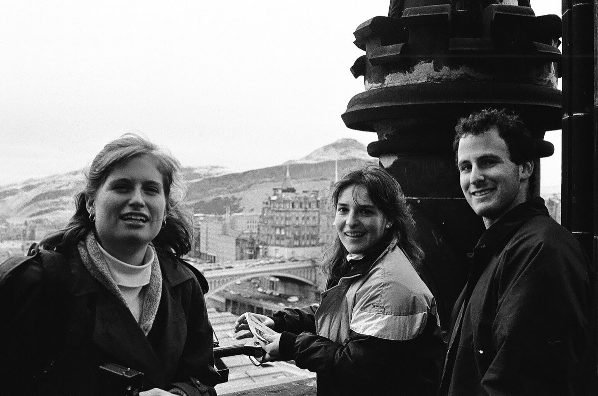Three students at the top of the Scott Monument, the North Bridge and Arthur's Seat behind them.
