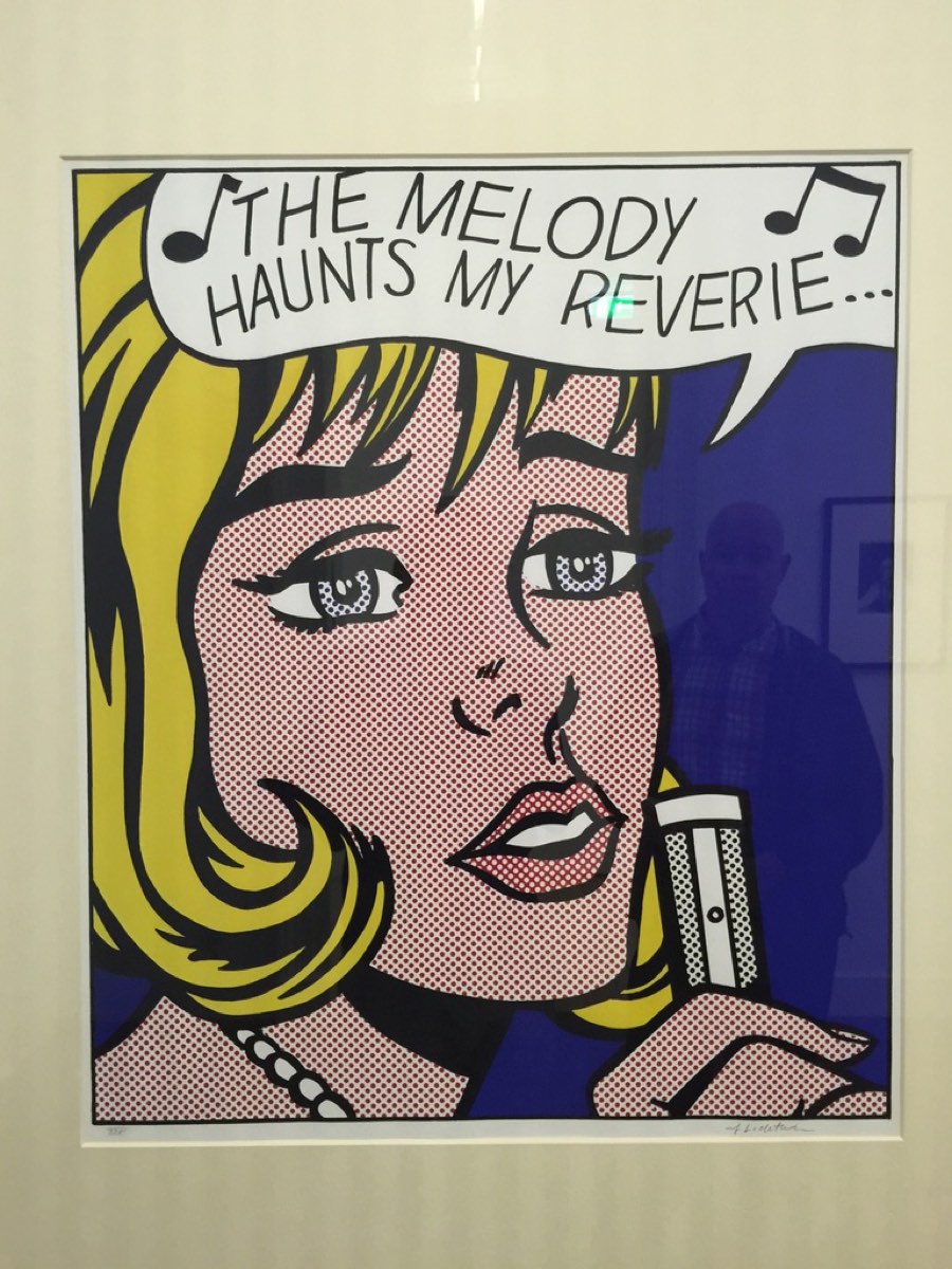 Roy Lichtenstein's print Reverie, a blonde woman with a microphone and the words The melody haunts my reverie, with a man reflected in the blue background.