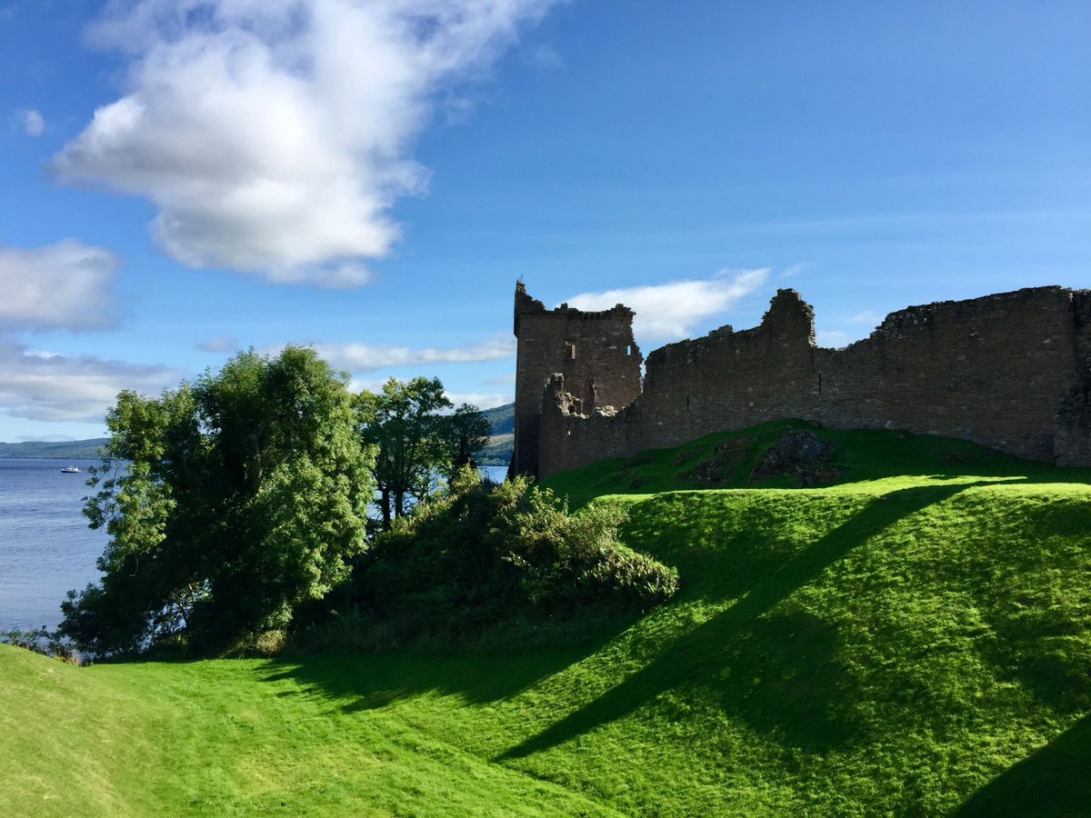 The ruined walls of Urquhart Castle on a bright green slope above Loch Ness.
